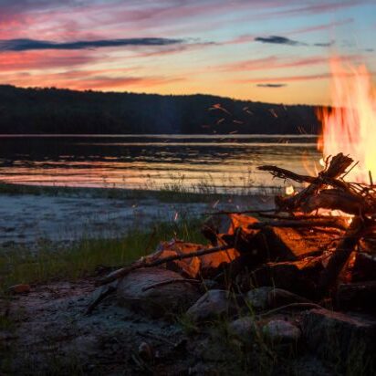 A fire burns in front of a lake at sunset