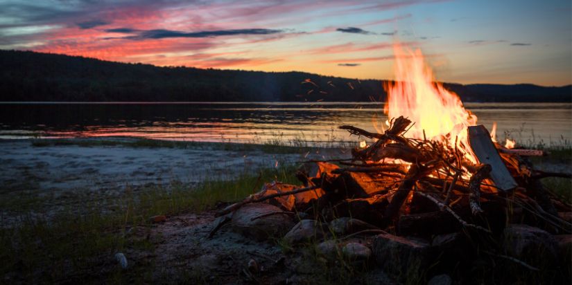 Camp Firewood from ProCut Firewood A fire burns in front of a lake at sunset