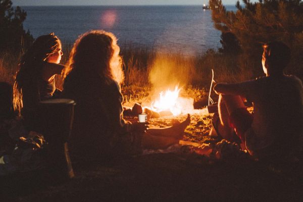 Three friends gather around a campfire on a beach